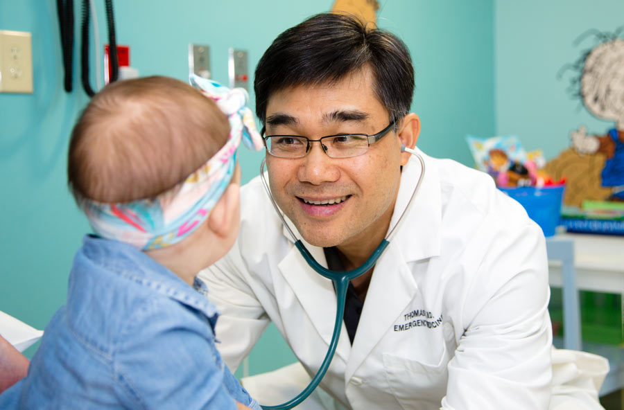 Tom Vo, M.D., smiles at a toddler in an exam room.