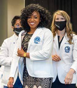 A woman smiles as she puts on her white coat for the first time.